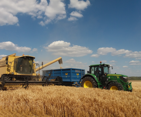 Close up of combine and tractor & trailer carting corn from the field